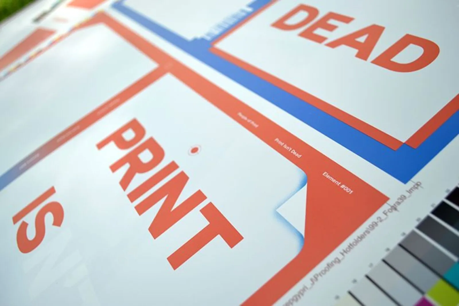 A printed press sheet with large red-orange letters and colour control bars at the edge of the sheet