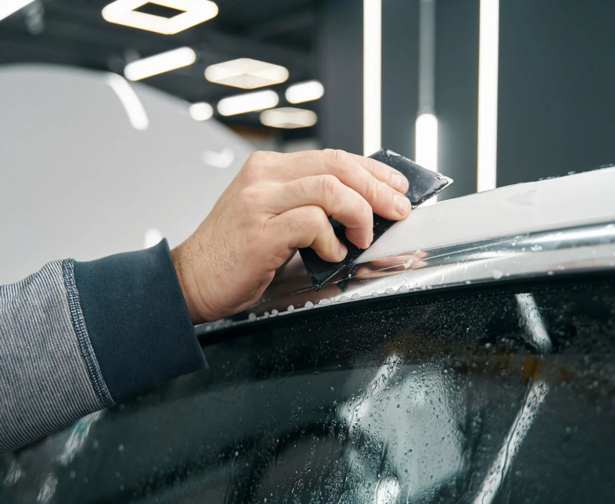 Installer applying vinyl wrap to a car roof with a squeegee
