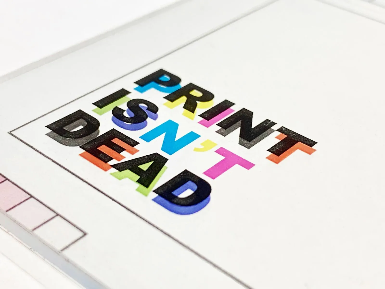 Bold colourful letters spelling PRINT ISN'T DEAD in overlapping colours printed on white paper