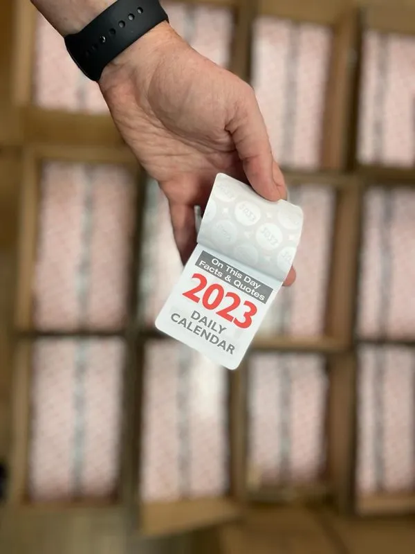 Printed 2023 tear-off daily calendar held up in front of boxed stock - Print Ready