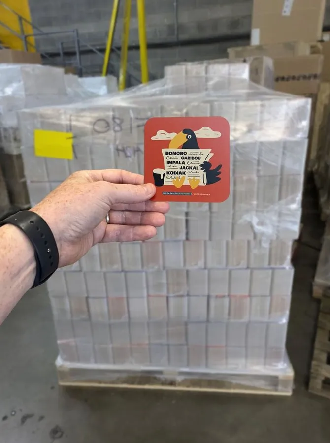 Printed beermat held up in front of a pallet of beermats
